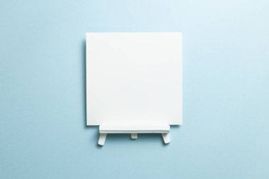 Mavi zemin üzerinde boş tuval olan beyaz sehpa. Üst görünüm, boşluk kopyala