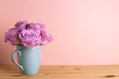Ahşap masada pembe arka planda seramik fincanda mor gül çiçekleri. Bahar çiçeği aranjmanı, kopyalama alanı