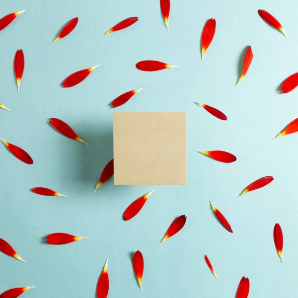 Kraft memo pad, empty paper with red flower petals on blue background. Floral composition, flat lay, top view, copy space