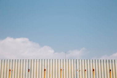 Gökyüzü mavisi arka planlı gri, dalgalı metal bir duvar.