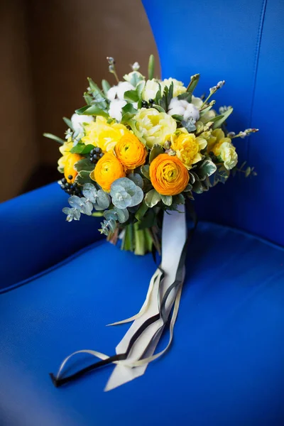 A large beautiful bouquet of lisianthus, cotton, eucalyptus, tulips, beautiful yellow, orange and white roses on an old leather armchair in bright blue