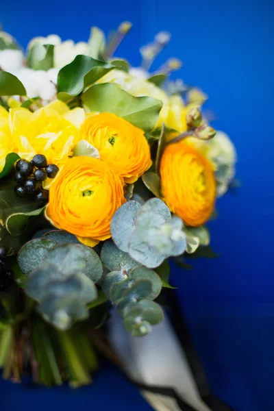 A large beautiful bouquet of lisianthus, cotton, eucalyptus, tulips, beautiful yellow, orange and white roses on an old leather armchair in bright blue
