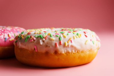 İki sulu taze tatlı çörek, üzerine şeker kreması ve pembe bir arka plan serpiştirilmiş.