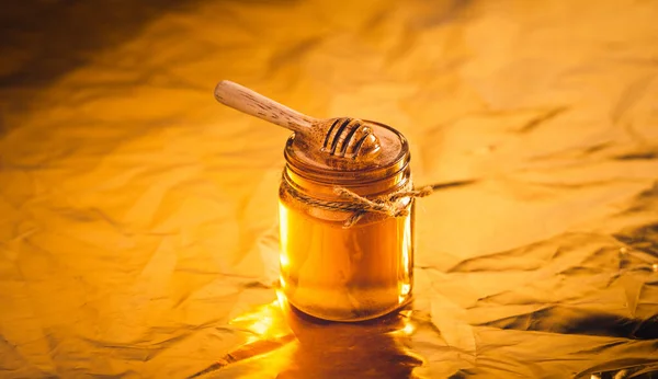 Golden honey in a glass bottle and golden background,Honey scoop