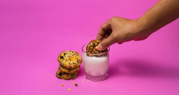 Cereal cookies and milk in a glass on a pink background