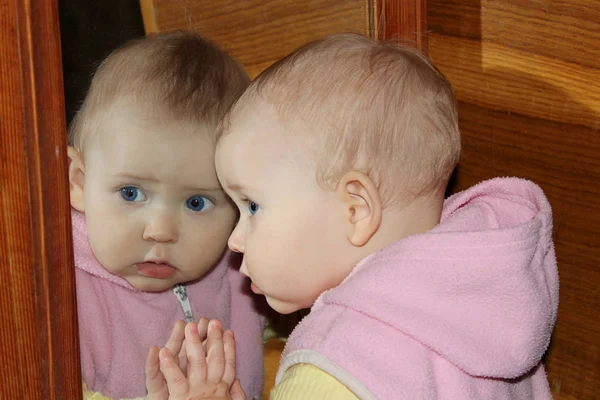 Bebê olha para si mesma na frente do espelho — Fotografia de Stock