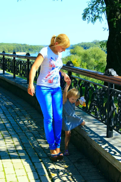 Modieuze vrouw leidt haar dochtertje bij de hand op de stoep in het park — Stockfoto