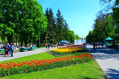 İnsanlar çiçek yatak ve çeşmeler ile parkta yürüyüş