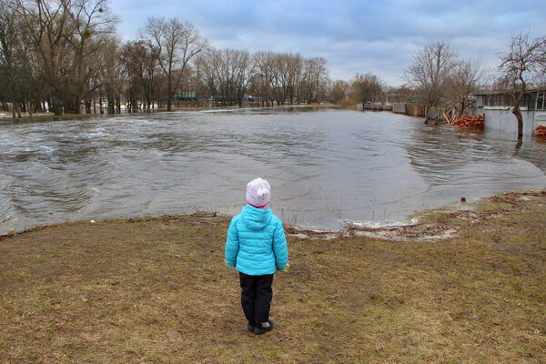 Child watching river flooding in city after melting snow in spring. Natural disaster