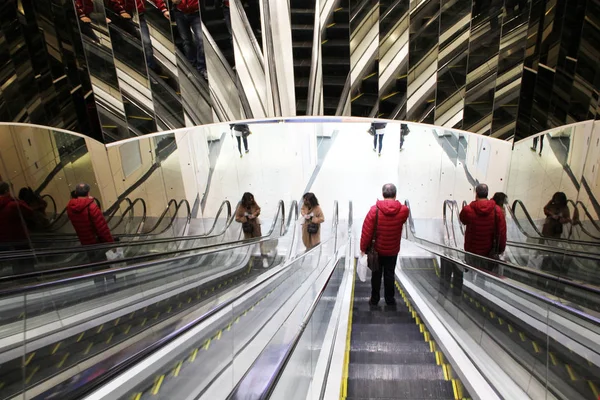 La gente monta escaleras mecánicas con paredes espejadas en el centro comercial —  Fotos de Stock