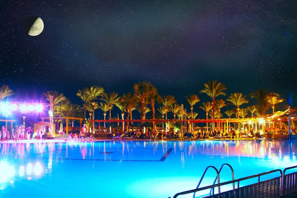 Měsíc nad bazénem s modrou vodou. Lidé si odpočinou v pětihvězdičkovém hotelu — Stock fotografie