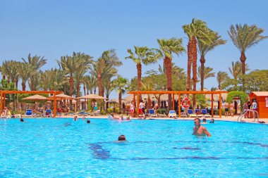 Hurghada / Mısır. 30 Temmuz 2018: Turistler Mısır 'daki havuzda tropikal tatil beldesinde dinlenmenin keyfini çıkarıyorlar. Açık mavi palmiye ağaçları olan yüzme havuzu. İnsanlar Mısır tatil köyünde dinleniyor. İnsanlar tatilleri yüzme havuzunda dinlenerek severler.