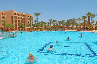 Hurghada / Mısır. 02 Ağustos 2018: Turistler Mısır 'daki havuzda tropikal tatil beldesinde dinlenmenin keyfini çıkarıyorlar. Açık mavi palmiye ağaçları olan yüzme havuzu. İnsanlar Mısır tatil köyünde dinleniyor. İnsanlar tatilleri yüzme havuzunda dinlenerek severler.