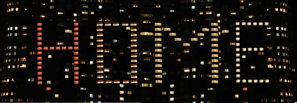 Word home composed of lighted windows in nocturnal high-rise building. Illuminated windows in shape of Home in block of flats. Inscription home on house of lighted windows on skyscraper at night
