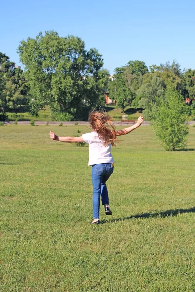女孩在草坪上跳起来 幼稚的感情快乐的孩子在夏天的草坪上开心的跳起来 在城市公园的绿草上跳着长发的小女孩 — 图库照片