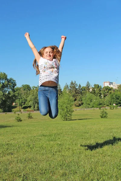 女の子は芝生でジャンプします 子供の感情 幸せな子供は夏の芝生で楽しくジャンプしています 若いです女の子とともに長いです髪ジャンプオン緑の草で都市公園 — ストック写真