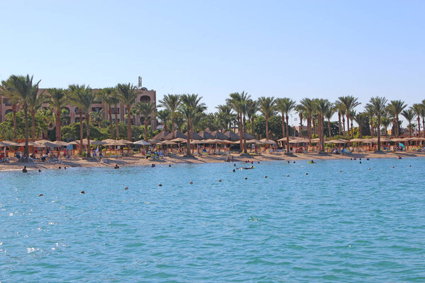 Hurghada / Egypt. 30 July 2018: Tropical resort in Egypt. People swimming in sea. Tourists relax on beach. People enjoy vacations on seaside resort at Red sea. Rest in Hurghada hotel Egyptian resort