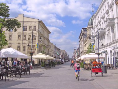 Lodz / Polonya. 18 Temmuz 2019: Bisikletli turist şehir caddesinde triportörün yanında. Gençler şehirde yürüyor ve bisiklete biniyor. Rickshaw, Lodz 'un merkez caddesinde ilerliyor. Şehir caddesinde üç tekerlekli bisiklete binen adam. Şehirde bisikletçi var.