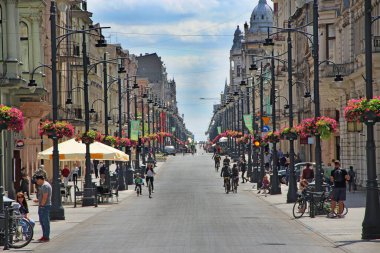 Lodz / Polonya. 18 Temmuz 2019: Birçok çiçek ve bisiklet süren insanların bulunduğu şehir caddesi manzarası. Lodz 'da şehir hayatı. Lodz Piotrkowska caddesinin merkez caddesi. Güzel bir şehir manzarası. Şehir hayatı. Panoramik şehir görünümü