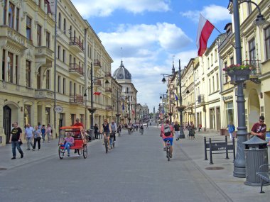 Lodz / Polonya. 18 Haziran 2019: Bisikletli turist şehir caddesinde triportörün yanında. Gençler şehirde yürüyor ve bisiklete biniyor. Rickshaw, Lodz 'un merkez caddesinde ilerliyor. Şehir caddesinde üç tekerlekli bisiklete binen adam. Şehirde bisikletçi var.
