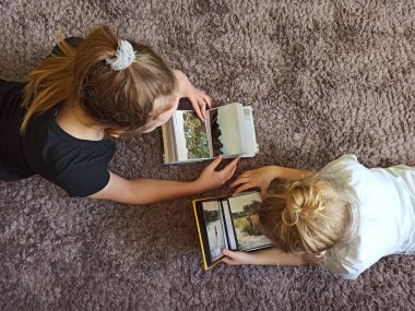 Küçük kız kardeşler evde harika vakit geçiriyorlar ve eski aile albümlerini izliyorlar. İki kız karantina sırasında eski fotoğraf albümlerine bakar. Çocuklar fotoğraf albümüne bakıyor. Çocuklar odada. Evde kalmak.