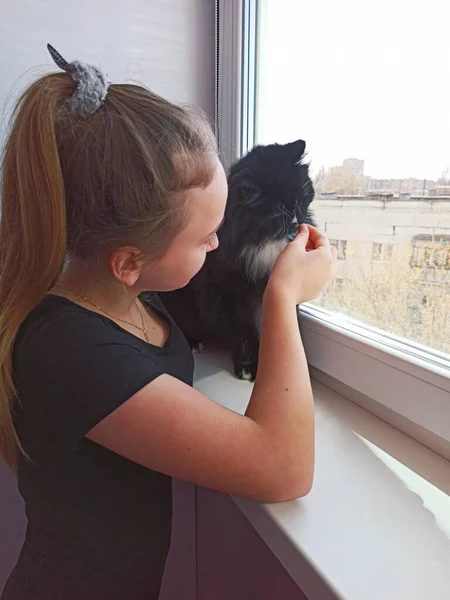 girl together with cat looking sadly out window staying home during quarantine because of coronavirus. Coronavirus quarantine concept. Sad child and cat at window-sill. Spending time during quarantine