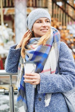 Kız gri ceket, şapka ve battaniye eşarp atlıkarınca yakınındaki kahve ile