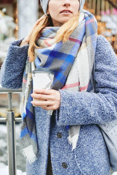 Девушка в сером пальто, шляпе и шарфе с чашкой кофе возле карусели — стоковое фото