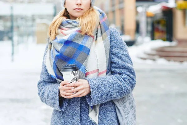 Girl in grey coat, hat and blanket scarf with cup of coffee on winter street — Stock Photo, Image