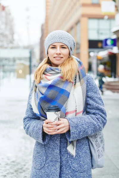 Dívka v šedý kabát, klobouk a deku šátek s šálkem kávy v zimě ulici — Stock fotografie