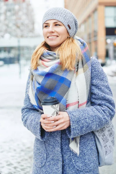 Девушка в сером пальто, шляпе и шарфе с чашкой кофе на зимней улице — стоковое фото