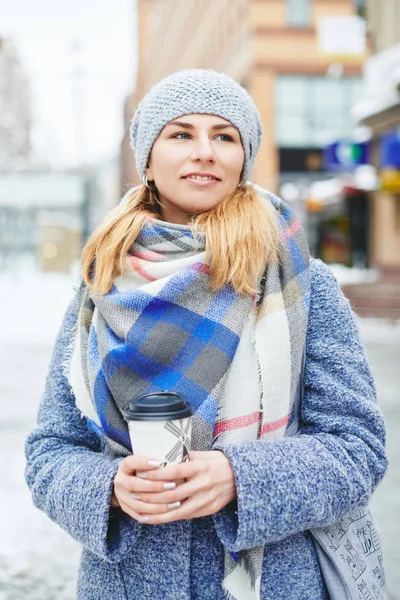 Девушка в сером пальто, шляпе и шарфе с чашкой кофе на зимней улице — стоковое фото