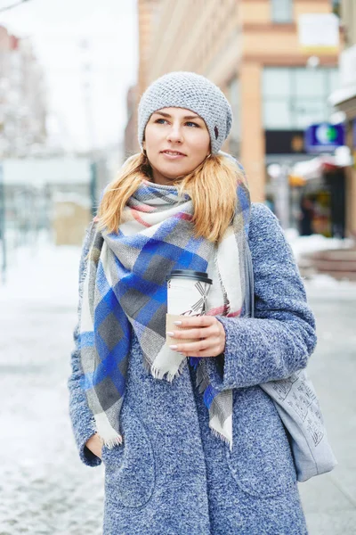 Dívka v šedý kabát, klobouk a deku šátek s šálkem kávy v zimě ulici — Stock fotografie