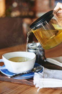 Kadın seramik kupa ahşap masa üzerinde içine yeşil çay cam çaydanlık dan yağıyor