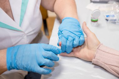 Doktor, bir damla kan almak için parmağını batırdıktan sonra glikoz seviyesini ölçüyor ve sonra dijital yapıştırıcı kullanıyor. Kıdemli diyabetik kadın evinde bölge hemşiresine muayene oluyor.