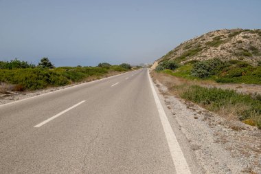 Yaz mevsiminde asfalt yolundaki yol ayrımını kapatın. Tepeli, tepeli, tepeli otoban yolundaki beyaz çizgiler. Yol yüzeyi. Asfalt yolda beyaz çizgi. Yaklaş ve açık mavi gökyüzü. Seyahat konsepti. Buradan görüntüle