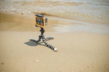 Küçük modern aksiyon kamerası, aksiyon kamerası deniz manzarasını kaldırır. Sahilde okyanus ve dalgaları kaydeden bir tripoda monte edilmiş aksiyon kamerası. Su geçirmez kasada kamera. Video blogcusu dışarıda 4K görüntü çekiyor..