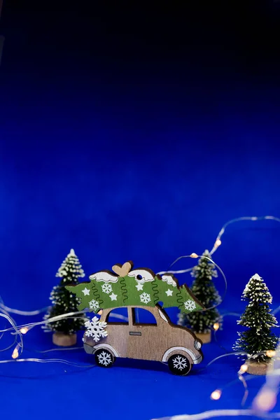 Carro de brinquedo com árvore de Natal e presente no telhado. Fundo azul com guirlanda. Ano Novo e Natal férias concept.New fundo festivo Ano, brinquedos vintage, árvore de Natal no fundo azul escuro com — Fotografia de Stock