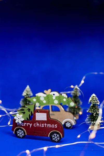 Carros de brinquedo de Natal com árvore de Natal no fundo azul, com fundo de feriado garland.New Year. Árvore de Natal no brinquedo de carro de madeira com fundo de árvore borrada. Natal celebração feriado, cópia — Fotografia de Stock