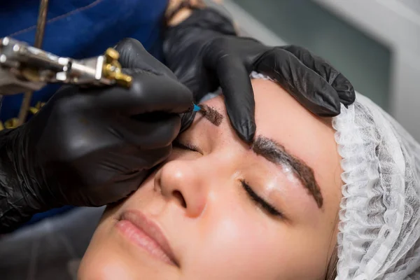Permanent Makeup For Eyebrows. Microblading brow. Beautician Doing Eyebrow Tattooing For Face. young girl with long eyelashes tweezing her brows in a beauty salon.permanent makeup eyebrows, tattooing