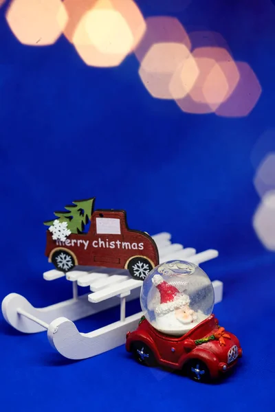 Kleines rotes Holzspielzeugauto auf blauem Hintergrund mit glänzendem Bokeh-Hintergrund. Weihnachten und Neujahr Feiertagsfeier Konzept. Festliche Dekoration und Hintergrund für Grüße mit copy space.creative — Stockfoto