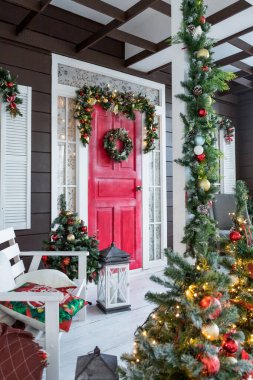 Kırmızı beyaz böğürtlenli Noel çelengi, ahşap kırmızı kapılı yıldızlar. Evin ön kapısında güzel bir çelenk. Klasik stil. Şık Noel sokak dekorları, şenlikli dekorasyonlar ve