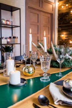 Şenlikli akşam yemeği. Çam kozalaklı dallar ve yanan beyaz mumlarla klasik şamdanlar. Zarif bir Noel veya şık cam, çatal bıçak seti ve Noel toplarıyla yeni yıl sofrası.