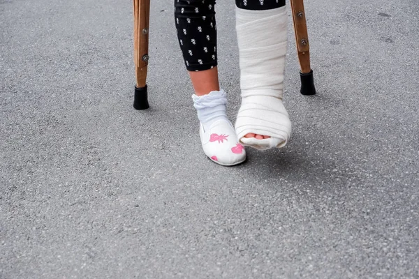 松葉杖を持つ少女が屋外を歩く。石膏の足で松葉杖の上のcast.childのSchool.legに戻ります。スペースをコピーしてはいけません。松葉杖の女の子彼女は足を骨折した. — ストック写真