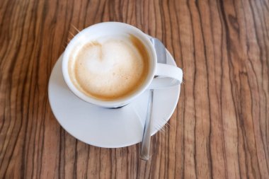 Beyaz kapuçino, ahşap arka planda latte sanatıyla birlikte. Güzel köpük, seramik kupa, fotokopi alanı. Sıcak içecek, ahşap masa arkasında güzel latte sanatıyla kapuçino kahvesi. Sabah içkileri.