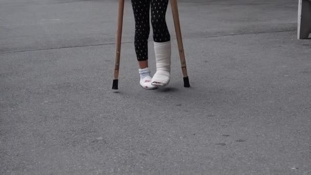 Barn med bruten fotled promenader med kryckor och gips gjutna på gatan. gjutna på barn fot. Går utomhus. En olycka, en bruten fotled. Selektiv inriktning. — Stockvideo