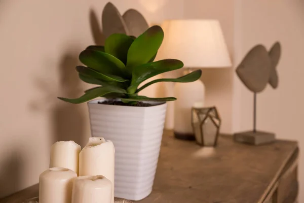 Una candela bianca, una lampada e una piccola pianta in vaso sono posizionati sul tavolo nella camera da letto.Candele, arredamento e pianta verde in vaso bianco sul tavolo in elegante appartamento elegante.home decor. Interior design . — Foto Stock