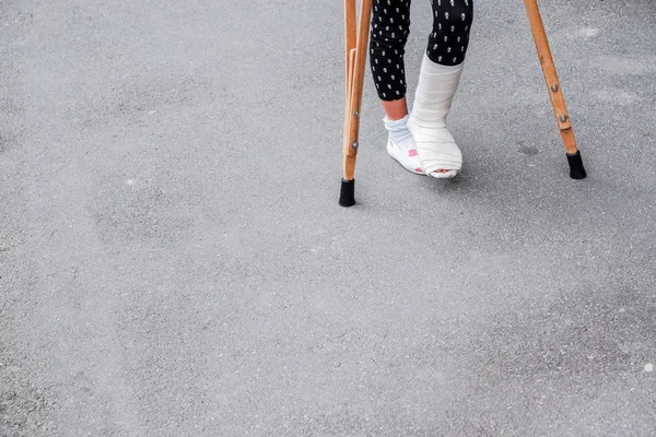 Egy gyerek mankóval és törött lábbal sétál a szabadban, közelről. Törött láb, fából készült mankó, bokasérülés. Csonttörés és bokatörés. beteg mankóval sétálni szabadban — Stock Fotó