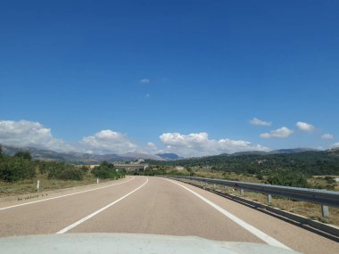 Boş bir dağ yolu görünüyor. Sağ taraftaki trafik. Hareket eden araba. Avrupa 'da arabayla seyahat. Güneşli bir günde güzel bir tepe manzarası. Dağ virajlı yolda araba kullanmak. İspanya, İtalya