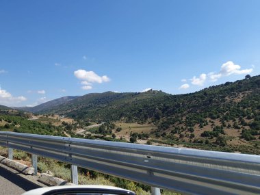 Boş bir dağ yolu görünüyor. Sağ taraftaki trafik. Hareket eden araba. Avrupa 'da arabayla seyahat. Güneşli bir günde güzel bir tepe manzarası. Dağ virajlı yolda araba kullanmak. İspanya, İtalya